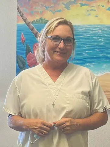 Dental Assistant Susanne smiling in front of an ocean-themed mural at Nick Dental Clinic.