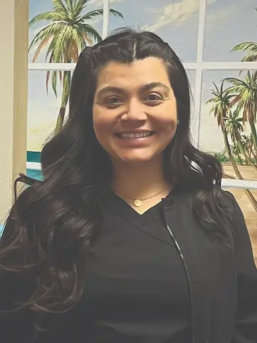 Registered Dental Hygienist Mimi smiling in front of a beach-themed wall at Nick Dental Clinic.